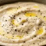 Best Alfredo Sauce Recipe for Pasta Lovers 7 Creamy Alfredo sauce in a pan with melted butter, heavy cream, and freshly grated parmesan cheese being stirred with a wooden spoon