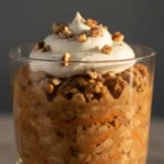 Carrot cake overnight oats layered in a glass and topped with whipped yogurt and chopped nuts.