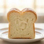Soft condensed milk bread with a fluffy interior and golden-brown crust on a wooden surface.