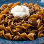 Ground Beef Stroganoff on blue ceramic plate with spiral pasta, seasoned ground beef, and dollop of sour cream on top
