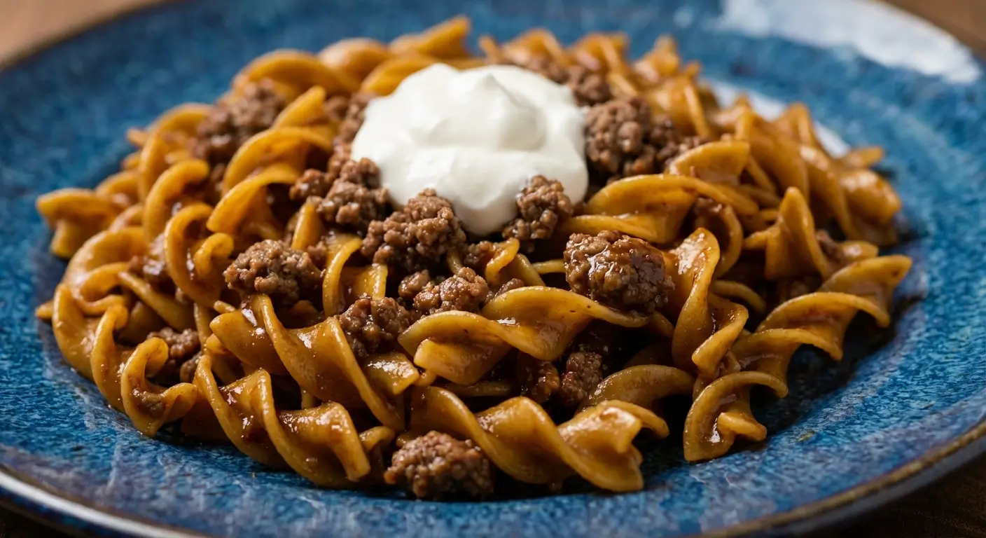 Ground Beef Stroganoff on blue ceramic plate with spiral pasta, seasoned ground beef, and dollop of sour cream on top