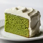 Slice of matcha green tea cake with white frosting on a white plate.