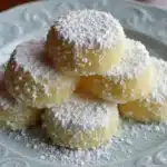 Meyer Lemon Meltaways (Quick and Easy) 7 Meyer Lemon Meltaways cookies stacked on a blue decorative plate, coated in thick powdered sugar with pale yellow centers visible