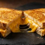 Tuna melt sandwich cut in half on black slate board showing golden-brown toasted bread with melted cheddar cheese stretching between halves and tuna salad filling