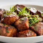 Air fryer steak bites seared and juicy, garnished with herbs and served hot on a plate.