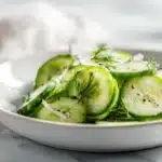 Fresh cucumber salad with thinly sliced cucumbers, onions, herbs, and light vinaigrette served chilled in a bowl.