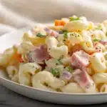 Macaroni Salad with Ham and Cheese 7 Macaroni salad with ham and cheese mixed with tender pasta, diced vegetables, and creamy dressing in a serving bowl.
