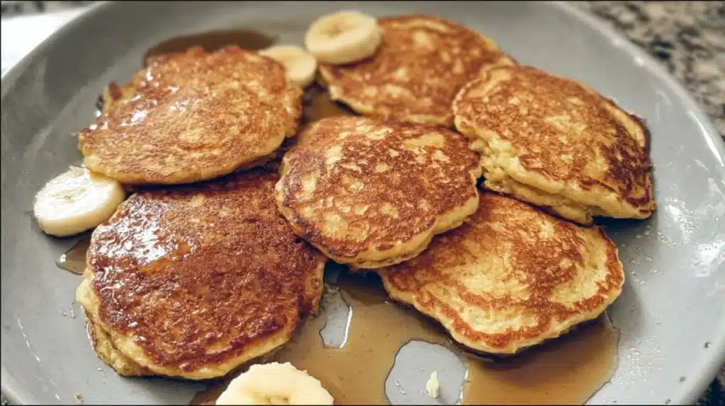 Stack of fluffy banana pancakes topped with sliced bananas and maple syrup, homemade breakfast pancakes served warm on a plate.