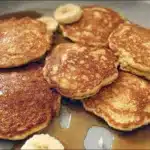 Stack of fluffy banana pancakes topped with sliced bananas and maple syrup, homemade breakfast pancakes served warm on a plate.