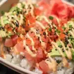 California Roll Sushi Bowls 6 California roll sushi bowl with crab, avocado, cucumber, rice, sesame seeds, and drizzled spicy mayo in a bowl.