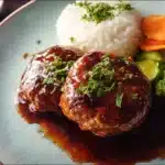 Japanese Hamburg Steak 6 Japanese Hamburg steak served with rich brown gravy, tender juicy beef patty, and a side of vegetables on a plate.