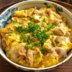 Steaming bowl of Oyakodon with glossy chicken, egg, and onion over fluffy rice, topped with scallions and pickled ginger.