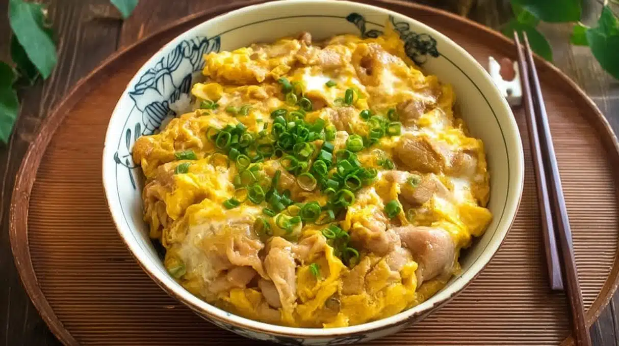 Steaming bowl of Oyakodon with glossy chicken, egg, and onion over fluffy rice, topped with scallions and pickled ginger.
