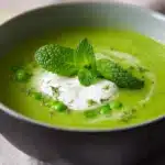 Creamy pea and mint soup served in a bowl, topped with fresh mint leaves and a drizzle of cream
