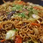 Yakisoba stir-fried noodles with cabbage, carrots, and sliced meat, coated in savory sauce and garnished with green onions.